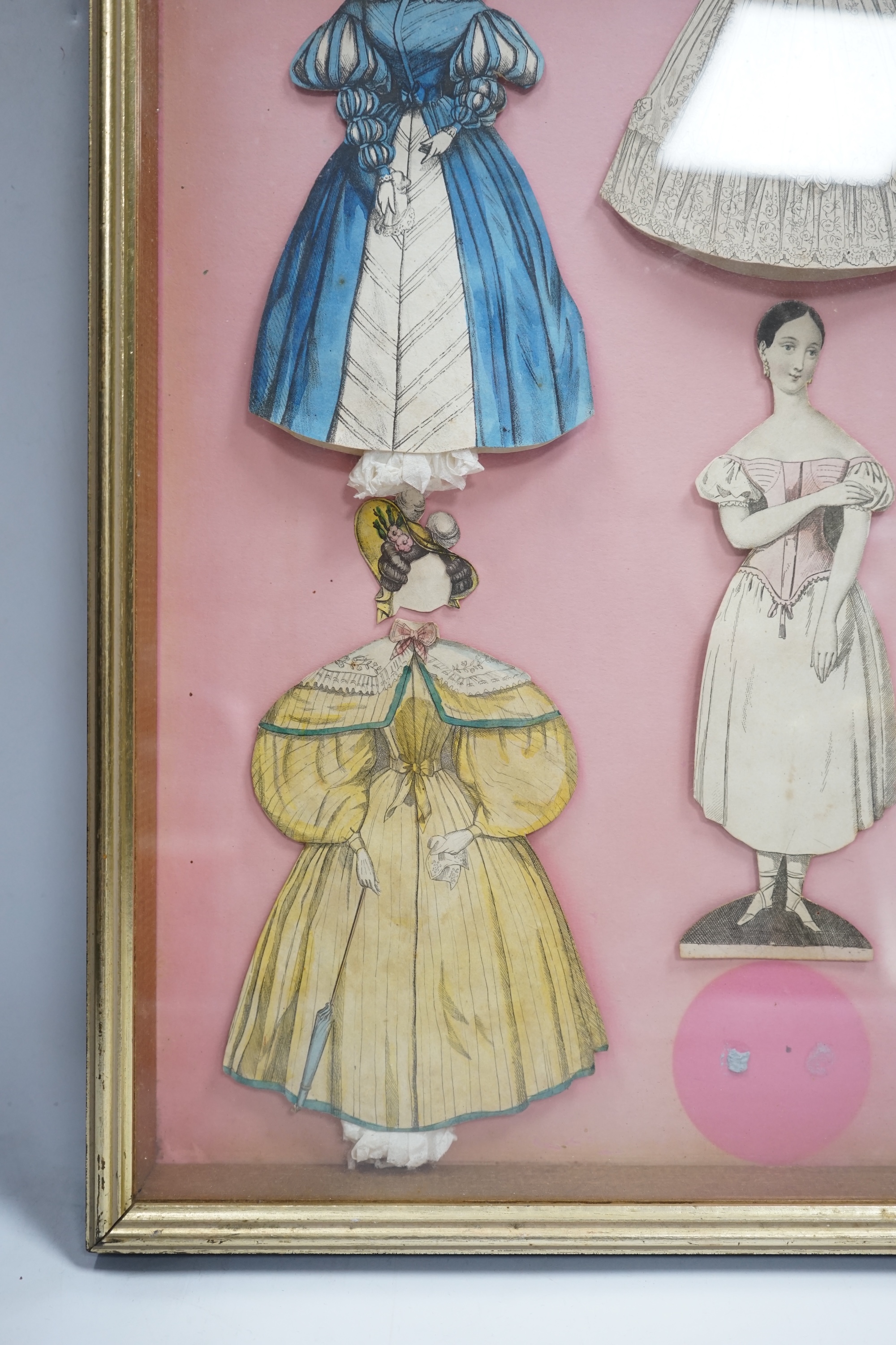 An early 19th century framed Rudolph Ackermann La Poupee-Modele paper doll set, comprising of a double sided doll in lingerie with wooden stand, five double sided gowns and five bonnets, dimensions of the frame; 40cm wid